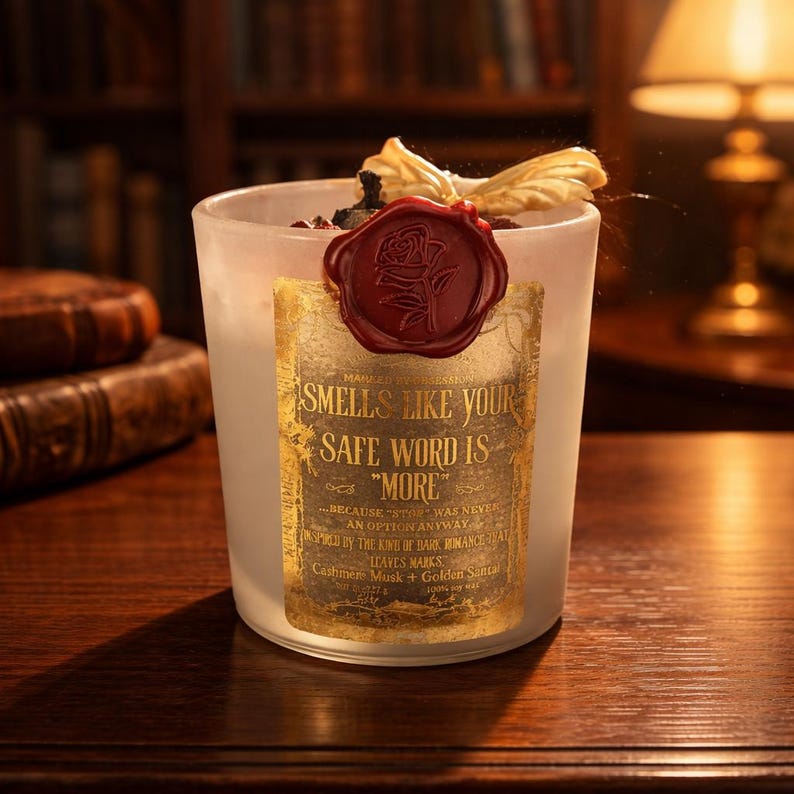 "Smells Like your safe word is "More"" 
Dark romance soy candle in matte white vessel with crimson wax bloom, golden wings, and gold foil label - Smells Like Your Safe Word Is More from Marked by Obsession collection