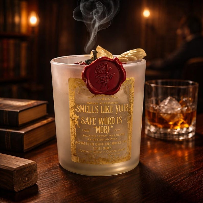 "Smells Like your safe word is "More"" 
Dark romance soy candle in matte white vessel with crimson wax bloom, golden wings, and gold foil label - Smells Like Your Safe Word Is More from Marked by Obsession collection