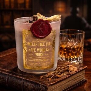 "Smells Like your safe word is "More"" 
Dark romance soy candle in matte white vessel with crimson wax bloom, golden wings, and gold foil label - Smells Like Your Safe Word Is More from Marked by Obsession collection