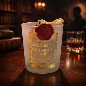 "Smells Like your safe word is "More"" 
Dark romance soy candle in matte white vessel with crimson wax bloom, golden wings, and gold foil label - Smells Like Your Safe Word Is More from Marked by Obsession collection