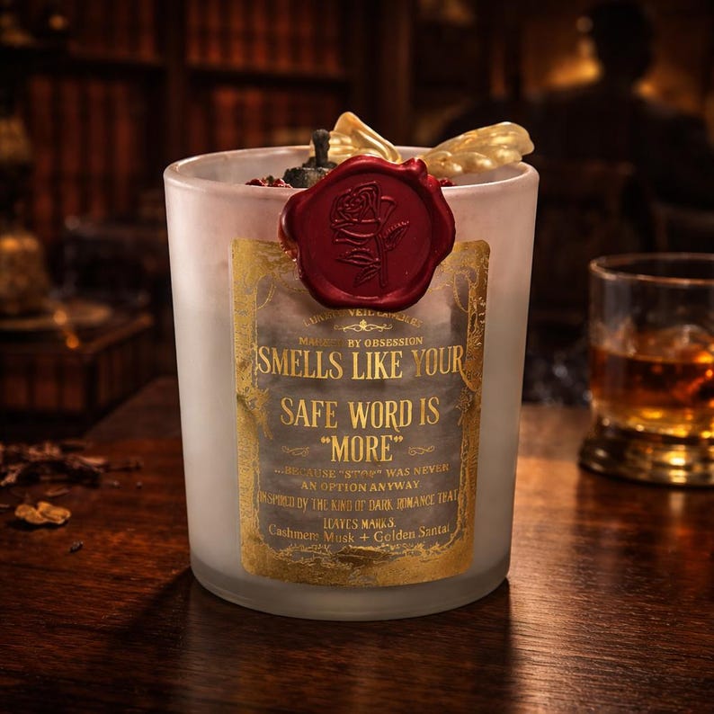 "Smells Like your safe word is "More"" 
Dark romance soy candle in matte white vessel with crimson wax bloom, golden wings, and gold foil label - Smells Like Your Safe Word Is More from Marked by Obsession collection