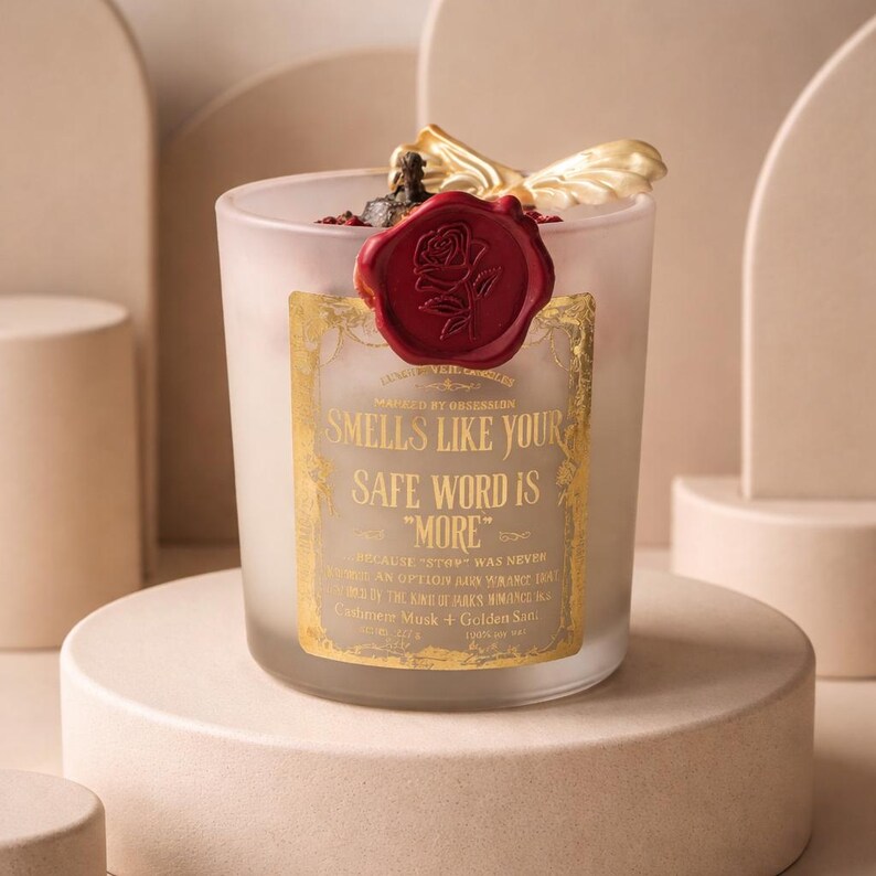 "Smells Like your safe word is "More"" 
Dark romance soy candle in matte white vessel with crimson wax bloom, golden wings, and gold foil label - Smells Like Your Safe Word Is More from Marked by Obsession collection