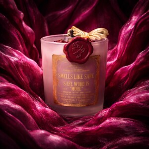 "Smells Like your safe word is "More"" 
Dark romance soy candle in matte white vessel with crimson wax bloom, golden wings, and gold foil label - Smells Like Your Safe Word Is More from Marked by Obsession collection
