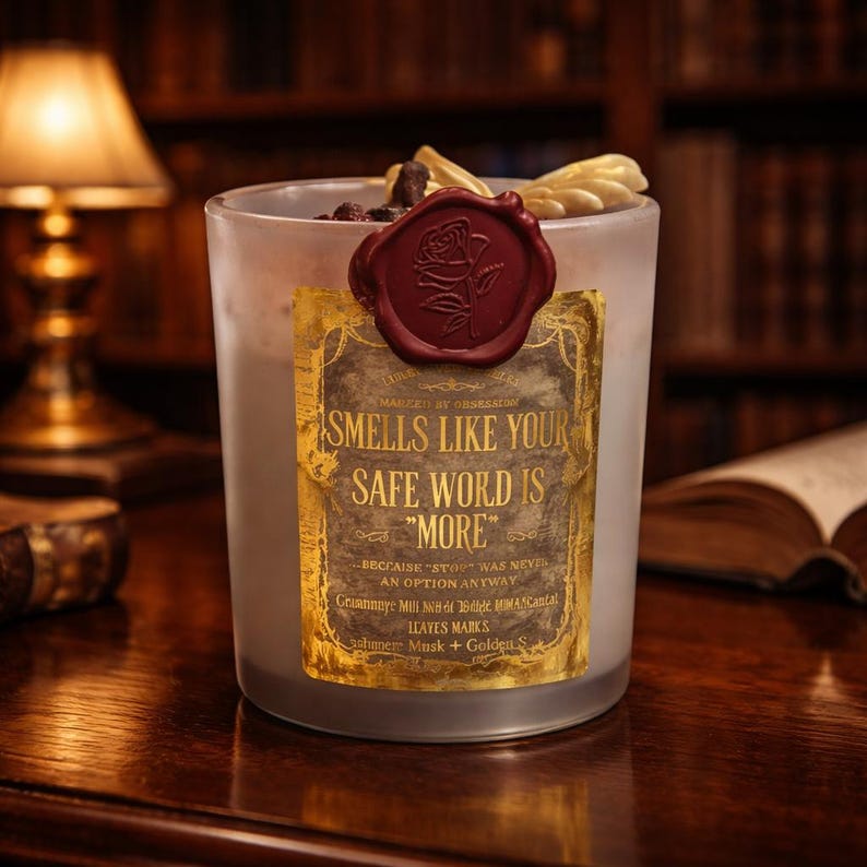 "Smells Like your safe word is "More"" 
Dark romance soy candle in matte white vessel with crimson wax bloom, golden wings, and gold foil label - Smells Like Your Safe Word Is More from Marked by Obsession collection