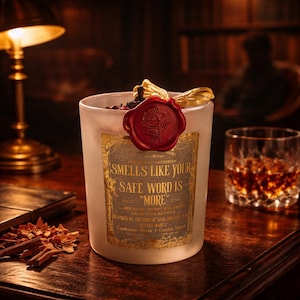 "Smells Like your safe word is "More"" 
Dark romance soy candle in matte white vessel with crimson wax bloom, golden wings, and gold foil label - Smells Like Your Safe Word Is More from Marked by Obsession collection