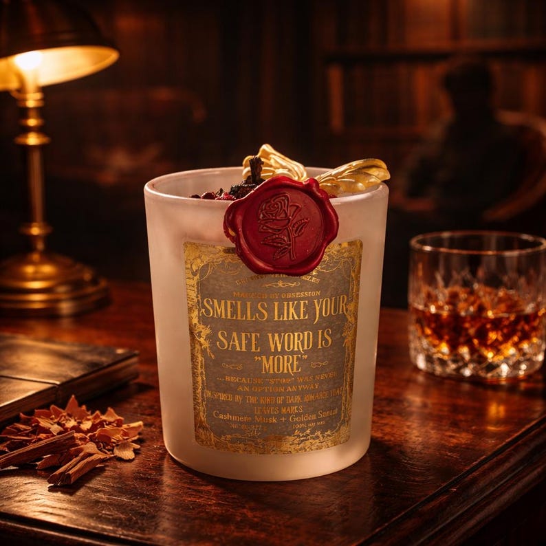 "Smells Like your safe word is "More"" 
Dark romance soy candle in matte white vessel with crimson wax bloom, golden wings, and gold foil label - Smells Like Your Safe Word Is More from Marked by Obsession collection
