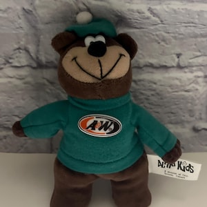 Könnte beinhalten: Ein brauner Plüschbär, der einen türkisfarbenen Pullover mit einem A&W-Logo auf der Brust und eine passende Mütze mit weißem Bommel trägt. Ein weißes Stoffetikett an der Seite zeigt die Aufschrift A&W Kids, A division of TRG, Toronto, Canada.