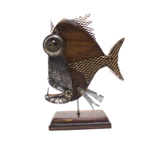 Könnte beinhalten: Eine dekorative Fischskulptur aus dunkelbraunem Holz und Metallkomponenten. Sie verfügt über ein großes kreisförmiges Auge, ein silbernes Netzgesicht, eine Metallflosse und einen Schwanz aus goldfarbenem Drahtgeflecht auf einem Holzsockel.