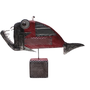 Könnte beinhalten: Eine Fischskulptur aus verschiedenen Metallkomponenten mit einem roten Körper, einem großen kreisförmigen Auge und spitzen Zähnen. Der Fisch ist auf einem dünnen Metallstab montiert, der an einem quadratischen Sockel mit Rautenmuster befestigt ist.