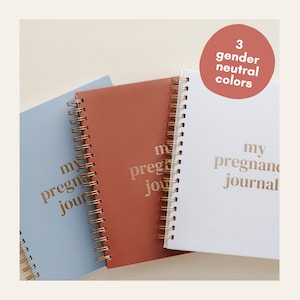 May include: Three spiral-bound journals in pastel blue, terracotta, and white. The words "my pregnancy journal" are printed in gold on the covers. A circular graphic states "3 gender neutral colours".