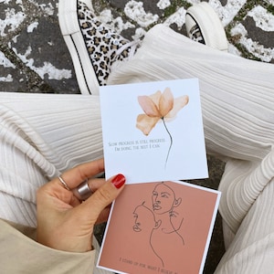 May include: Two inspirational cards with motivational quotes. The first card has a peach-colored flower and the text "Slow progress is still progress I'm doing the best I can". The second card has a peach background with a line drawing of two faces and the text "I stand up for what I believe in".