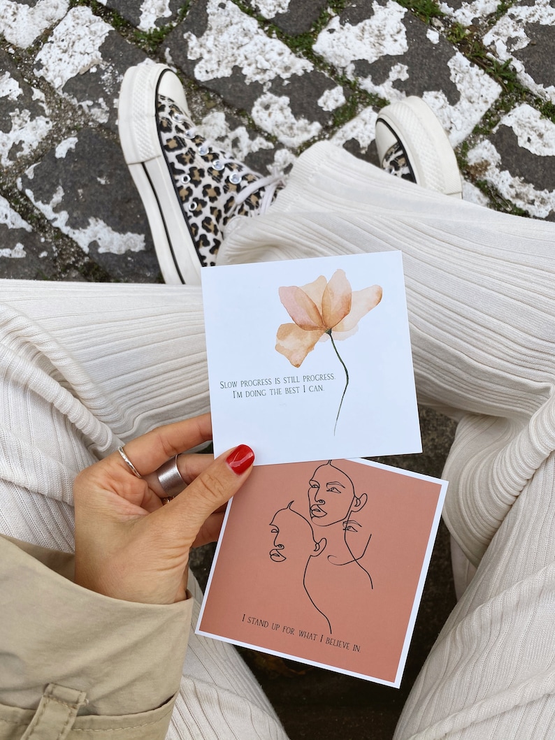 May include: Two inspirational cards with motivational quotes. The first card has a peach-colored flower and the text "Slow progress is still progress I'm doing the best I can". The second card has a peach background with a line drawing of two faces and the text "I stand up for what I believe in".