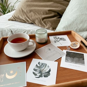 May include: A wooden tray with a white teacup, a candle, and five cards with inspirational quotes. The quotes are: "Today is a sacred gift from life", "I am in perfect balance", "I am worthy of all that I desire, only within each moment I live", "I trust my inner voice", and "I am worthy of all that I desire, only within each moment I live".