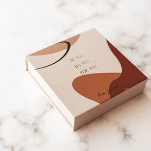 May include: A white box with a brown and beige abstract design. The box has the text "Be you. Do you. For you." and "From Lovemore" printed on it.