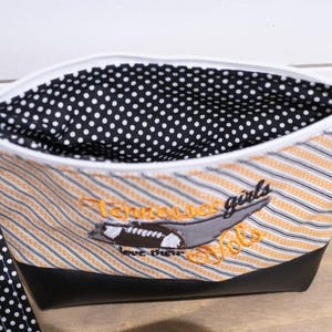 Op de afbeelding: Een zwarte en witte stippen-ritszak met een zwarte en oranje gestreepte buitenkant. De tas heeft een zwarte leren bodem en een zwarte en witte stippenband. De tas heeft een geborduurd ontwerp met een voetbal en de tekst "Tennessee girls love their Vols".