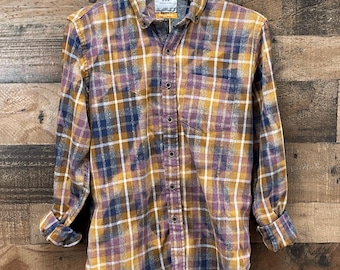 May include: A long-sleeve button-down shirt featuring a mustard yellow, navy blue, and white plaid pattern with a bleached, distressed effect. The shirt includes a single chest pocket, a standard collar, and a label reading MRK.