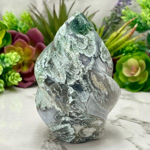 May include: A polished, freeform gemstone sculpture. The stone features swirling patterns of gray, white, and green. The sculpture has a smooth, undulating shape, and is a decorative item.