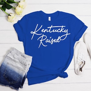 May include: A royal blue t-shirt with the text "Kentucky Raised" in white cursive lettering.