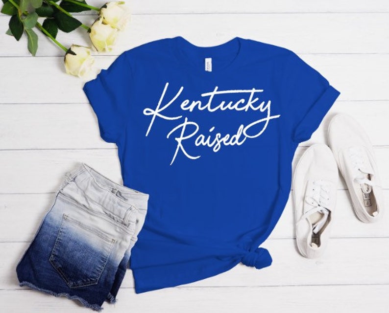 May include: A royal blue t-shirt with the text "Kentucky Raised" in white cursive lettering.