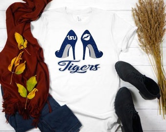 Peut inclure: T-shirt blanc avec un graphique bleu de deux talons hauts avec le texte "TSU Tigers" en dessous.