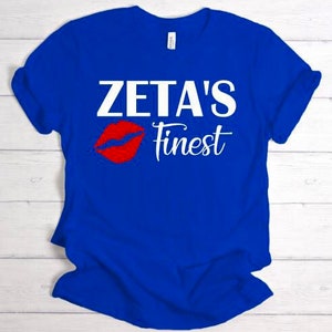 May include: A royal blue t-shirt with white text that reads "Zeta's Finest" and a red lip print.