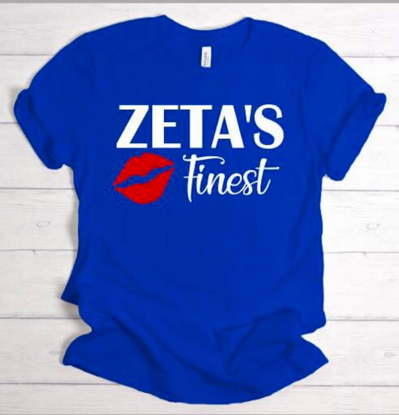 May include: A royal blue t-shirt with white text that reads "Zeta's Finest" and a red lip print.