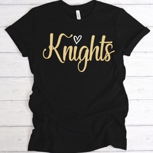May include: Black t-shirt with a gold inscription that reads "Knights" with a small white heart above the word.