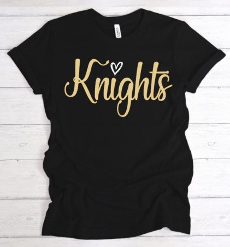 May include: Black t-shirt with a gold inscription that reads "Knights" with a small white heart above the word.