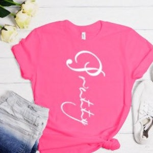 May include: A pink t-shirt with the word "Pretty" written in white cursive on the front.