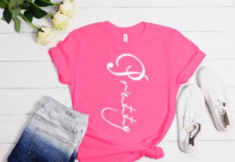 May include: A pink t-shirt with the word "Pretty" written in white cursive on the front.