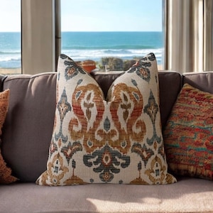 May include: A brown couch with two throw pillows. The couch is in front of a window with a view of the ocean. The throw pillows have a colorful geometric pattern.