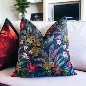 May include: A navy blue throw pillow with a floral pattern featuring pink, yellow, and green flowers. The pillow is on a white couch.
