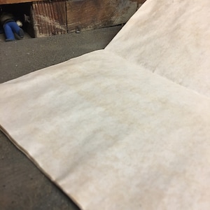 May include: A blank, off-white, paper notebook with a slightly rough texture. The notebook is open and lying flat on a dark, textured surface.