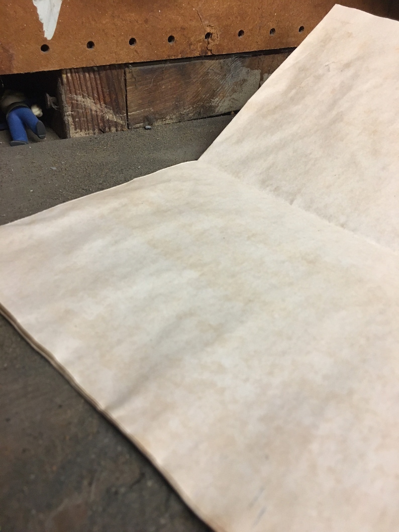 May include: A blank, off-white, paper notebook with a slightly rough texture. The notebook is open and lying flat on a dark, textured surface.
