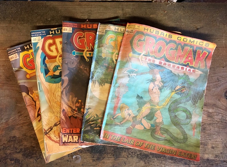 May include: A stack of vintage comic books featuring the character Grognak the Barbarian. The covers are colourful and feature illustrations of Grognak fighting mythical creatures. The text on the covers reads "Grognak the Barbarian" and "Hubris Comics".