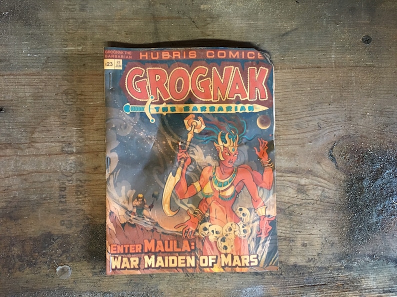 May include: A vintage comic book cover featuring a red-skinned female warrior with a sword and a skull-covered throne. The title is "Grognak the Barbarian" and the tagline is "Enter Maula: War Maiden of Mars".