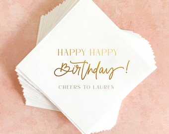 May include: A stack of white napkins with gold lettering that reads "Happy Happy Birthday! Cheers to Lauren".