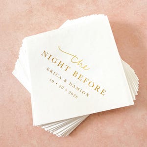 May include: A stack of square white paper napkins featuring gold foil text that reads the NIGHT BEFORE, ERICA & DAMION, and 10 20 2026. The design includes a decorative gold script flourish above the word the, centered on the top napkin.