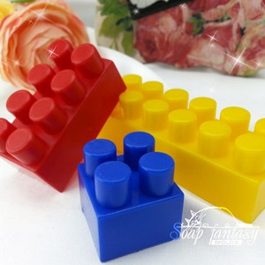 Puede incluir: Tres bloques de construcción de plástico de color rojo, amarillo y azul. Los bloques tienen forma de ladrillos LEGO tradicionales con tacos en la parte superior.