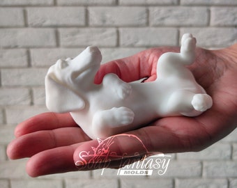 May include: White silicone mold of a dachshund dog laying on its back with its paws in the air. The mold is in a person's hand. The mold is for making soap, candles, or other crafts.