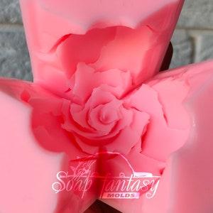 May include: Pink silicone mold shaped like a rose. The mold is open and shows the detailed rose design. The mold is labeled "Soap Fantasy Molds".