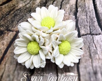 May include: A close-up of a white silicone mold of three daisy flowers with yellow centers. The mold is on a wooden background.  Soap fantasy molds.