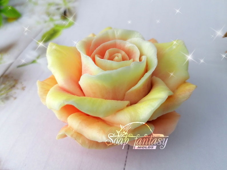 May include: A close-up of a handcrafted soap shaped like a rose. The soap features a gradient of colors, transitioning from yellow to peach and pink. The soap is labeled "Soap Fantasy Molds".