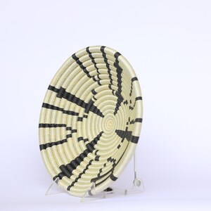 May include: A large, round woven basket with black and white stripes. The basket is made of natural materials and has a unique, geometric design.