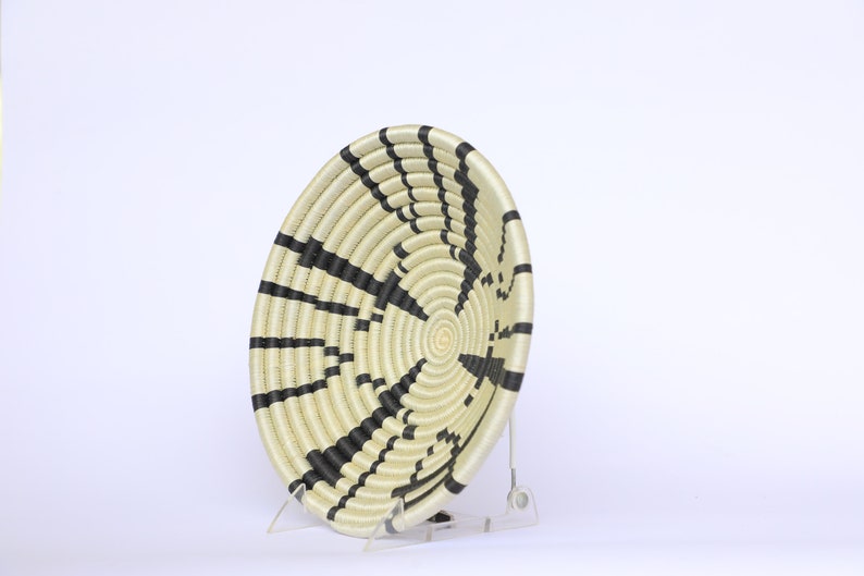 May include: A large, round woven basket with black and white stripes. The basket is made of natural materials and has a unique, geometric design.