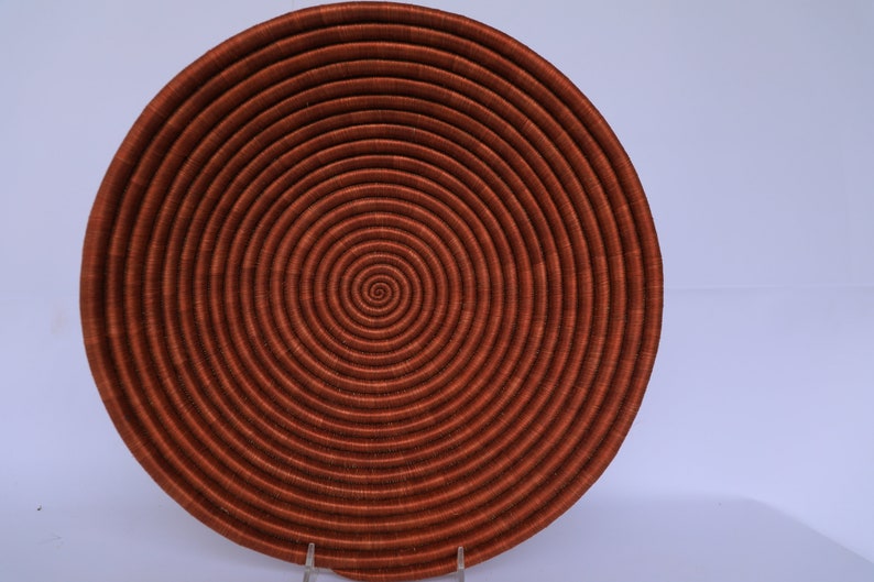 Pode incluir: Uma cesta grande, redonda e tecida com um padr&atilde;o em espiral. A cesta &eacute; feita de fibras naturais e &eacute; de cor castanho-avermelhado escuro.