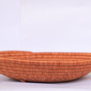 Pode incluir: Uma cesta grande, redonda e tecida feita de fibras naturais. A cesta &eacute; de cor castanho claro e tem uma textura lisa e uniforme. &Eacute; perfeita para guardar e exibir artigos.
