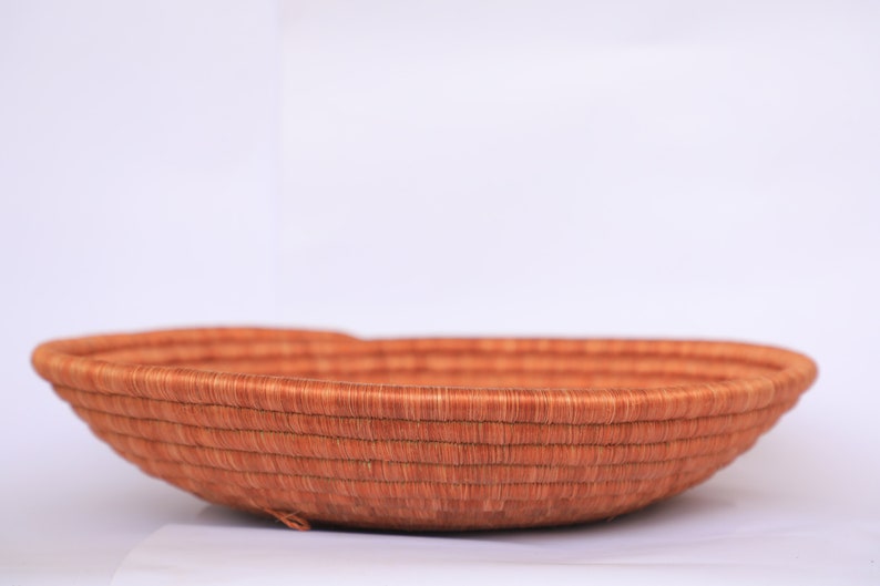 Pode incluir: Uma cesta grande, redonda e tecida feita de fibras naturais. A cesta &eacute; de cor castanho claro e tem uma textura lisa e uniforme. &Eacute; perfeita para guardar e exibir artigos.
