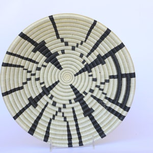 May include: A large, round woven basket with a black and white geometric pattern. The basket is made of natural fibers and has a circular shape.