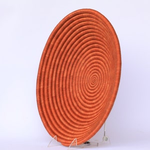 Pode incluir: Uma cesta grande, redonda e laranja tecida com um padr&atilde;o em espiral. A cesta &eacute; feita de fibras naturais e tem um aspecto r&uacute;stico e feito &agrave; m&atilde;o.